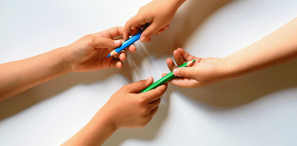 image of two children one left-handed and one-right handed exchanging colored pencils for a post on left-handed vs right-handed writing